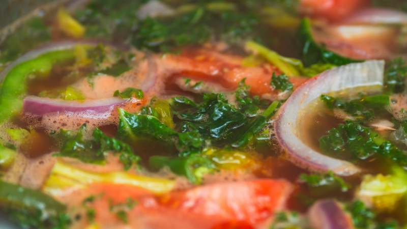 Steaming bowl of vibrant organic vegetable soup with fresh herbs on rustic wooden table